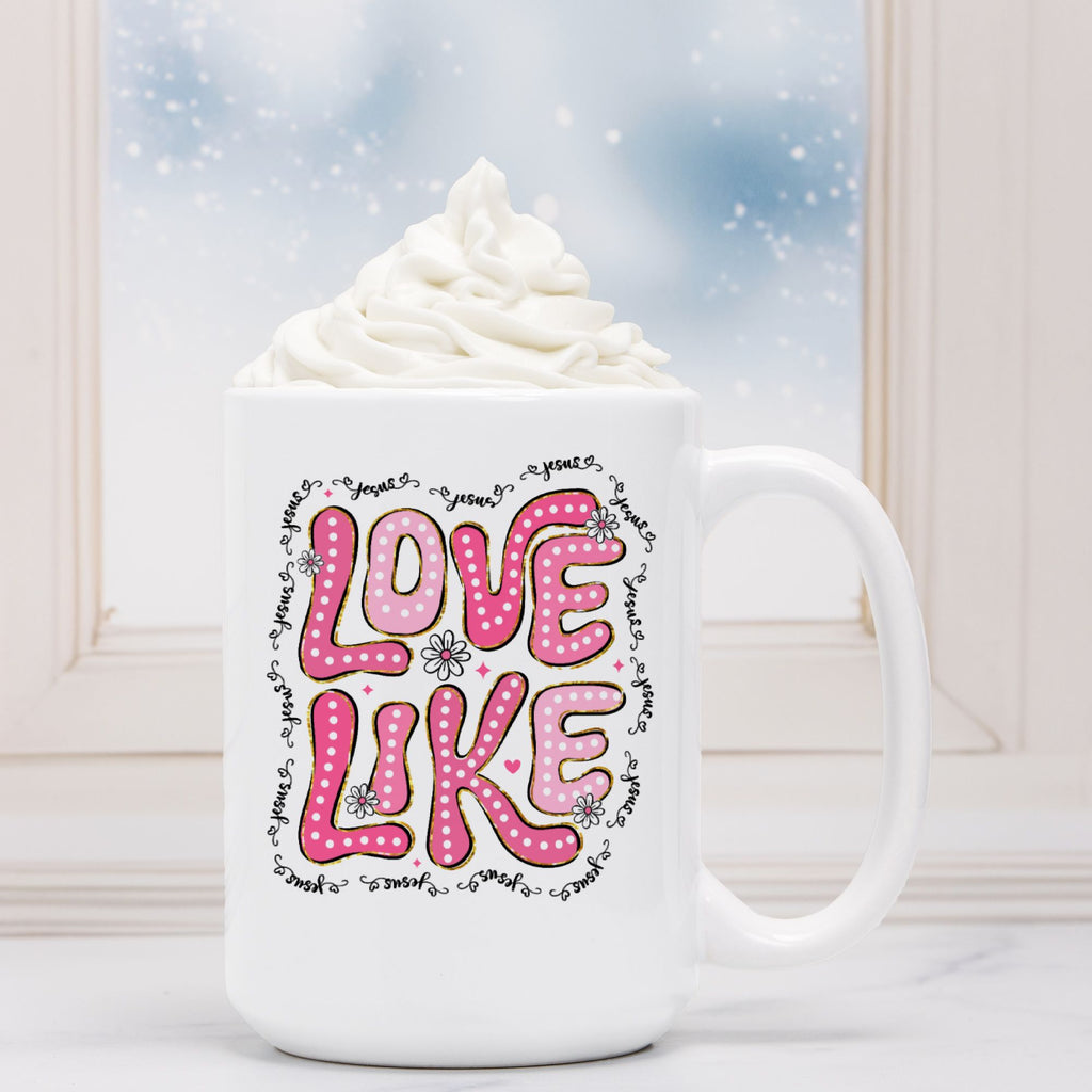 White mug with 'LOVE LIKE' text in pink, topped with whipped cream against a snowy window background.