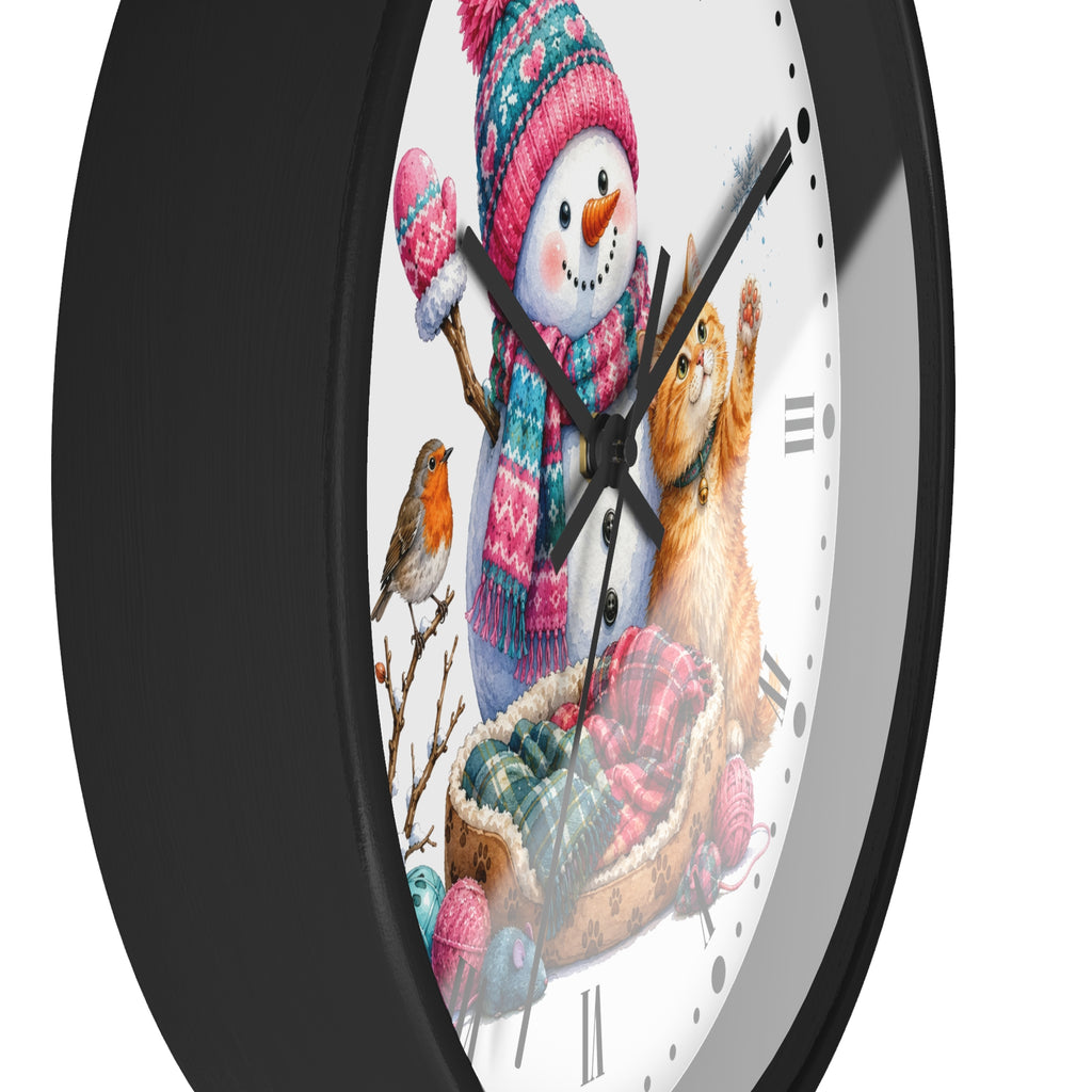 A round wall clock with a black frame and a white face featuring a winter illustration of a snowman, a cat, and a small bird, and colorful knit hats and scarves.