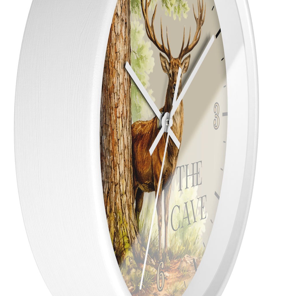 A white round wall clock with a printed forest scene featuring a deer by a tree and the words 'THE CAVE' on the dial.
