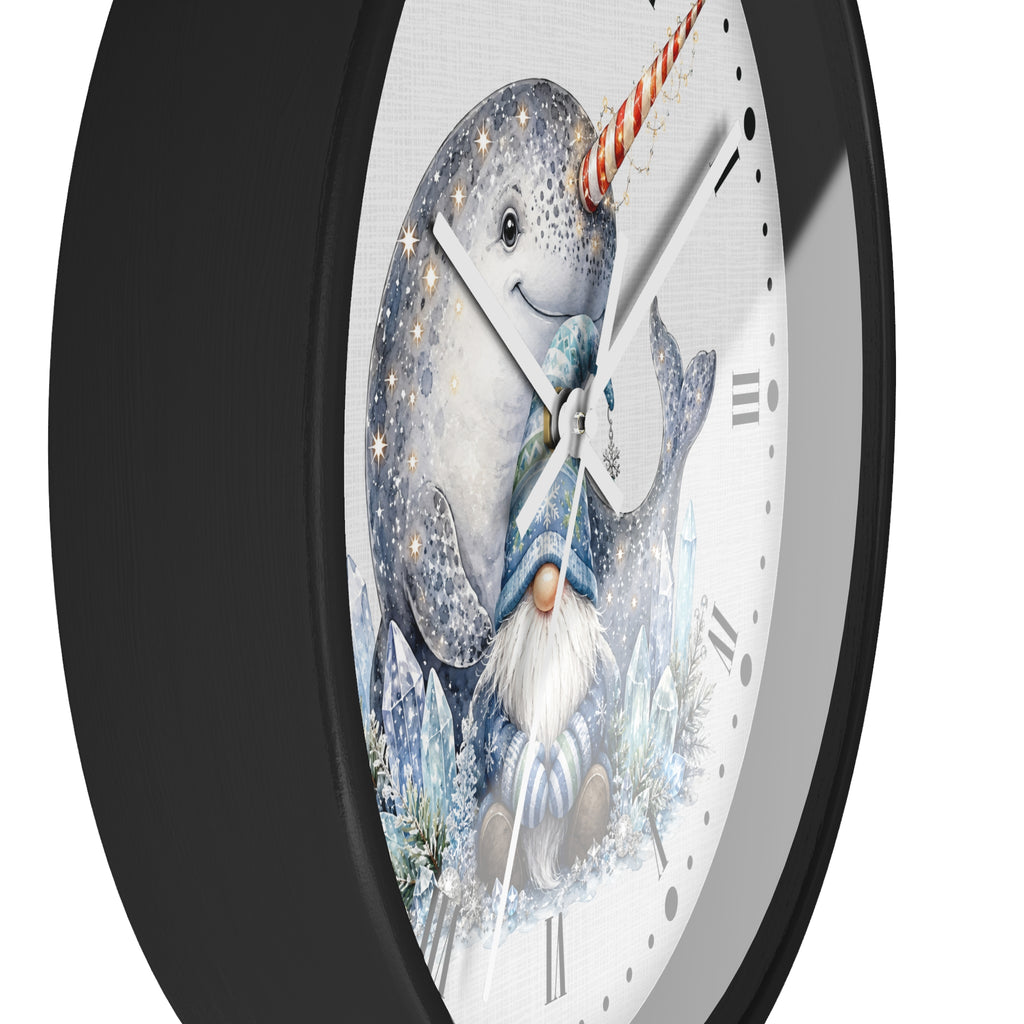 A close-up of a round wall clock with a black frame and a white dial featuring a whimsical illustration of a narwhal and a gnome in winter clothing.