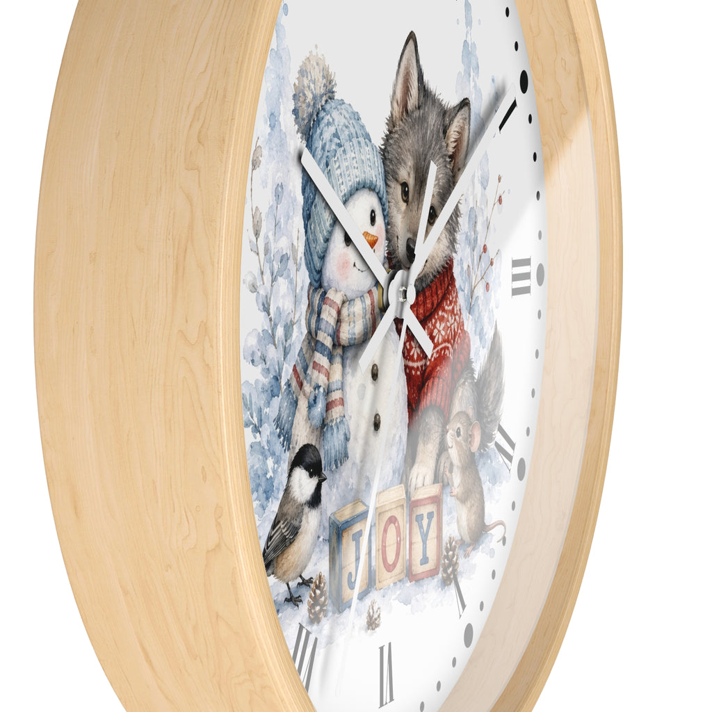 A round wall clock with a light natural wood frame and a white face featuring a winter illustration of a snowman, a wolf, a penguin, a chickadee, and the word "JOY" in colorful blocks.