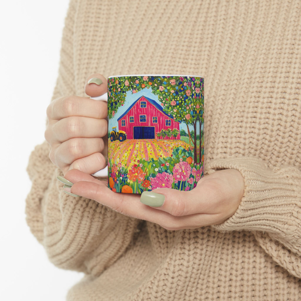 Person holding a mug with a colorful design of a red barn and garden.