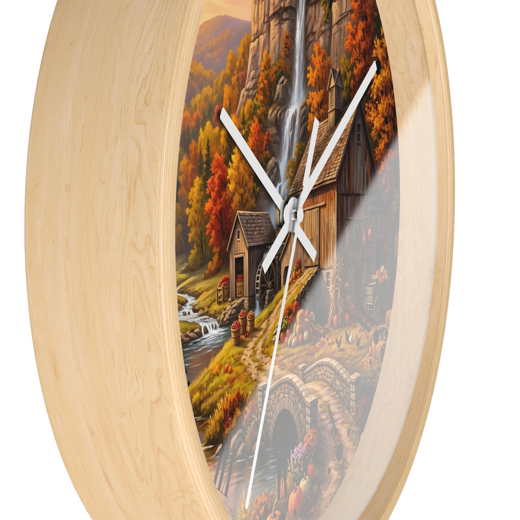Round wall clock with a light natural wood frame and a printed scenic artwork insert showing an autumn landscape with a waterfall, cabin, trees, and stone bridge.