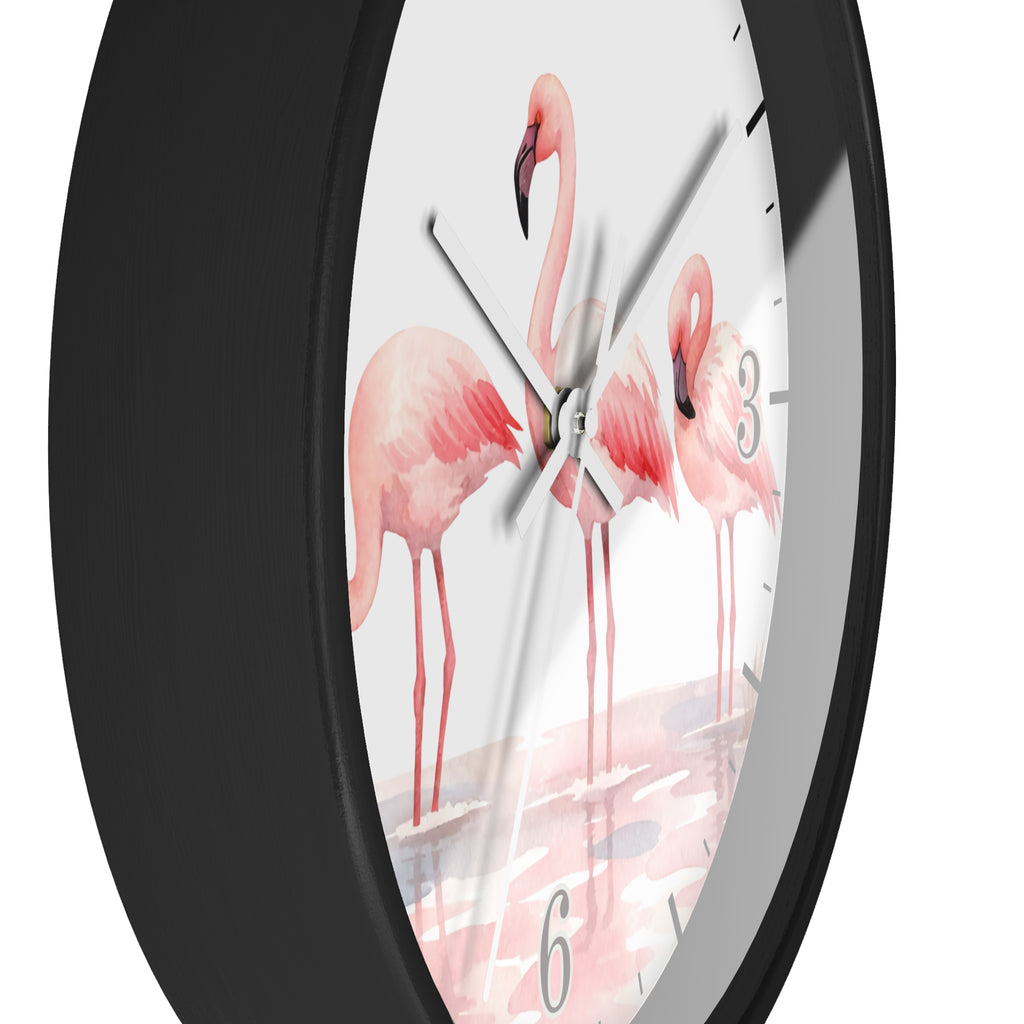 A close-up of a round wall clock with a matte black frame and a white dial printed with three pink flamingos standing in shallow water. The clock has black Arabic numerals and black hour markers, with silver-tone hands.