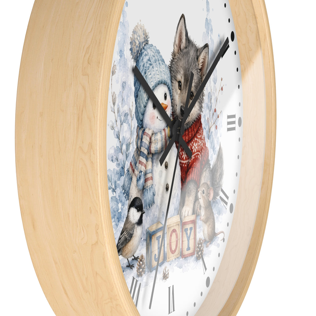 A round wall clock with a light natural wood frame and a whimsical winter illustration on the face. The artwork shows a penguin in a blue knit hat and scarf, a gray wolf in a red sweater, a small bird, a squirrel, and the word "JOY" in colorful blocks.