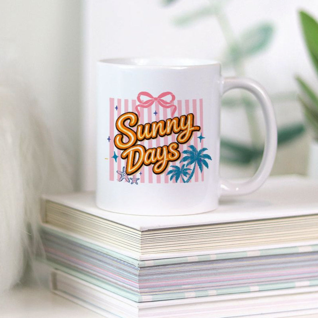 White mug with 'Sunny Days' design on a stack of books with plants in the background