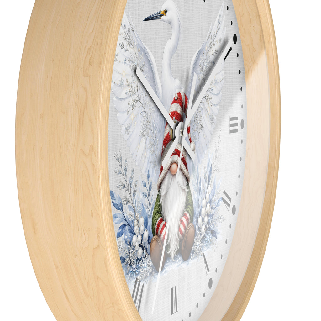 Round wall clock with a light natural wood frame and a white face featuring a winter scene of a white heron with wings spread, holding a gnome dressed in red and green striped clothing among blue snowy branches.