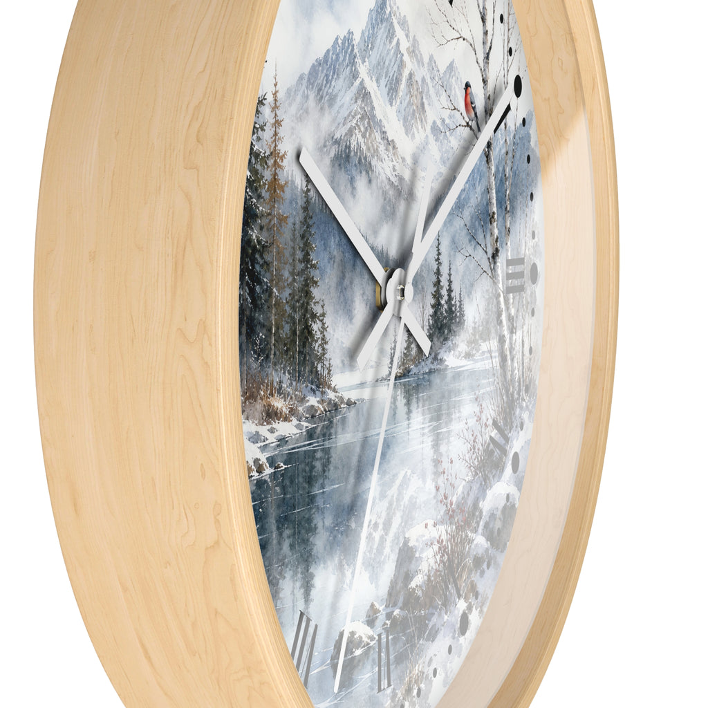 Round wall clock with a light natural wood frame and a printed winter landscape face showing snow-covered mountains, trees, and a frozen river, photographed on a white background.