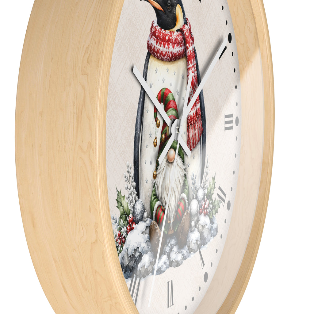 A round wall clock with a light natural wood frame and a festive winter illustration of a penguin wearing a red and white knit scarf, standing in the snow beside a small gnome.