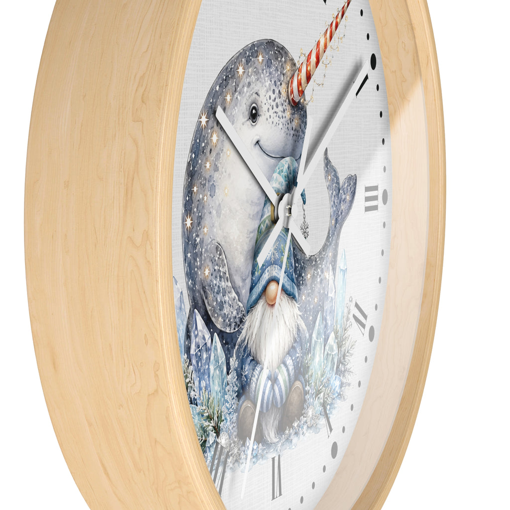 A round wall clock with a light natural wood frame and a white face featuring a whimsical illustration of a narwhal and a snow-covered gnome.