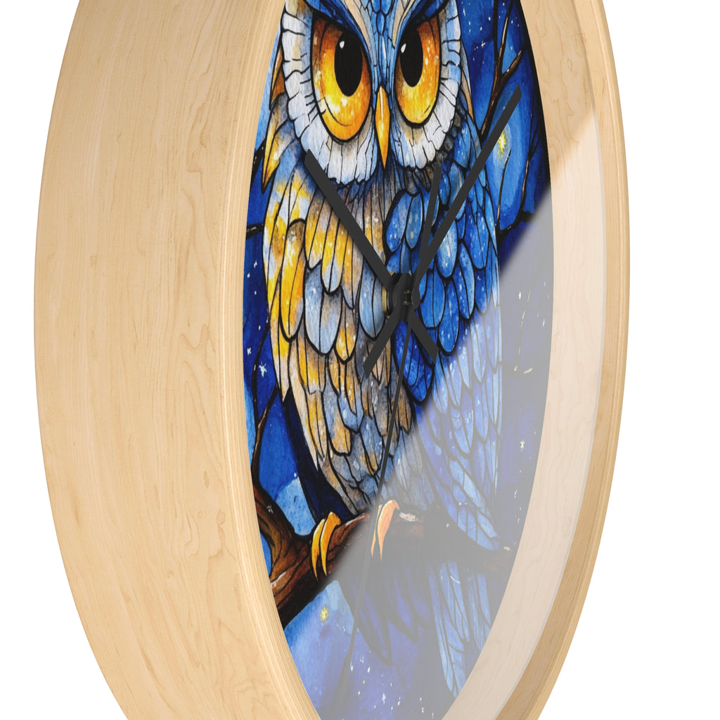 A round wall clock with a light natural wood frame and a colorful printed owl design on the face. The owl artwork features large yellow eyes, blue and white feathers, and a dark blue night-sky background.