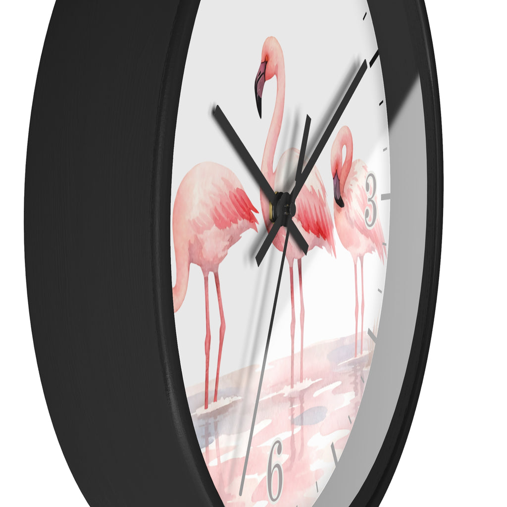 A close-up of a round wall clock with a matte black frame and a white dial printed with three pink flamingos standing in shallow water. The clock has black hands and gray Arabic numerals.