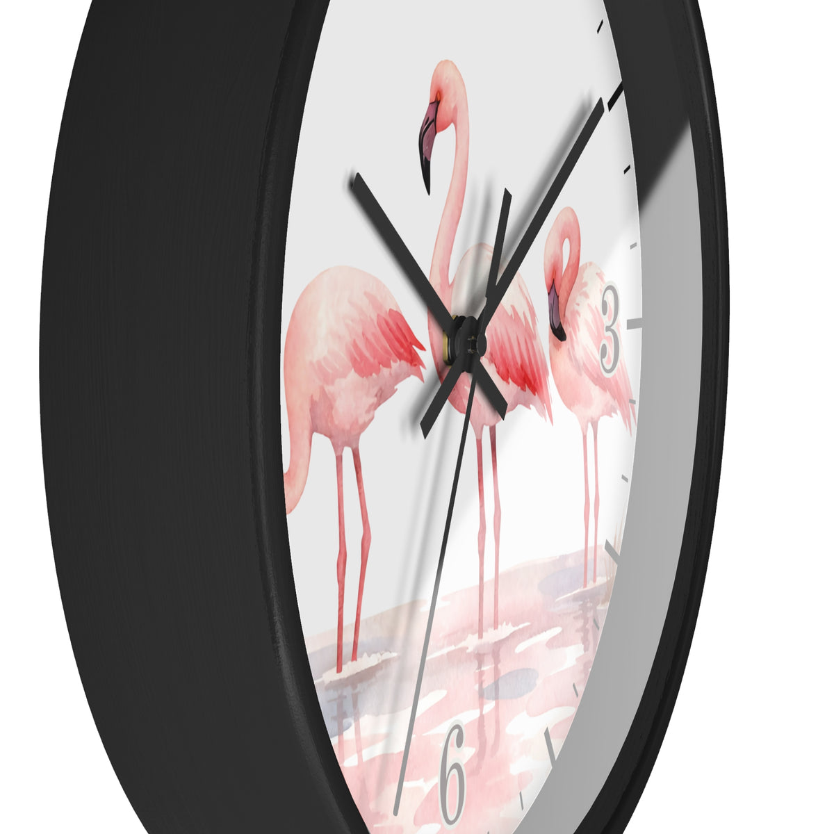 A close-up of a round wall clock with a matte black frame and a white dial printed with three pink flamingos standing in shallow water. The clock has black hands and gray Arabic numerals.