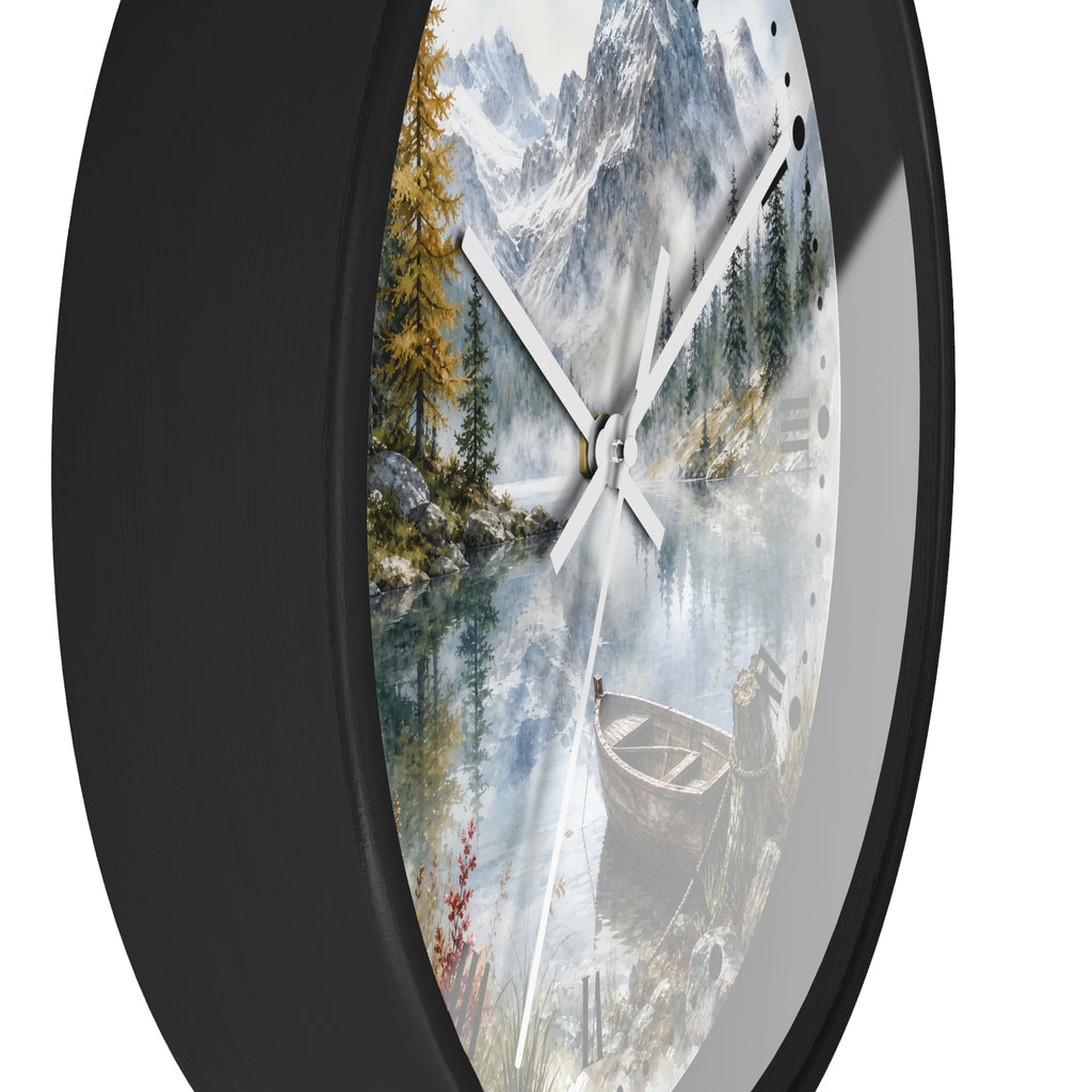 A round wall clock with a black frame and a scenic print of a mountain lake landscape featuring pine trees, a boat, and snowy peaks. The clock is shown at an angle against a plain white background.