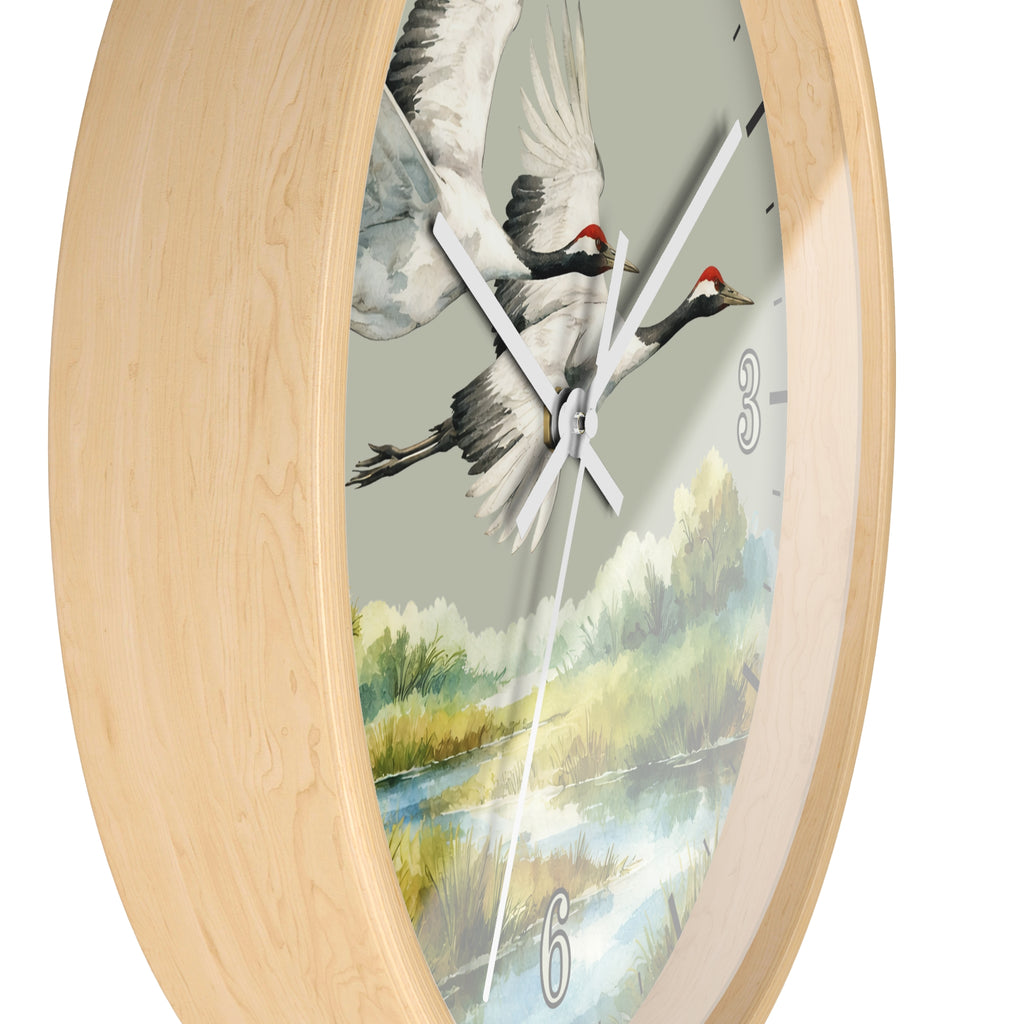 An oval wall clock with a light natural wood frame and a printed dial showing two flying cranes over a river landscape. The clock is photographed against a plain white background.
