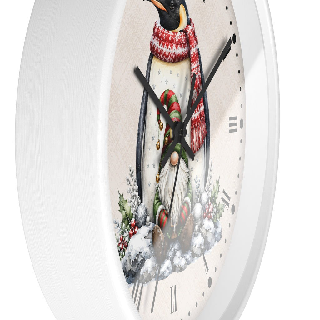A white round wall clock with a festive Christmas design on the face, featuring a penguin in a red and white striped scarf and a small gnome beneath it, shown against a plain white background.