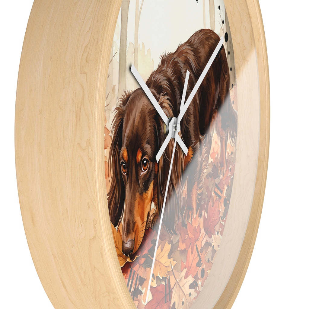 Round wall clock with a light natural wood frame and a printed center illustration of a brown dachshund dog walking among autumn leaves, with white clock hands.