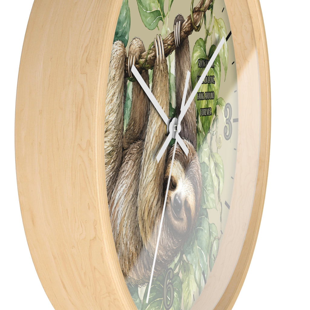 Round wall clock with a light natural wood frame and a printed face showing a sloth hanging from a rope among green leaves, with white hands and black numerals.