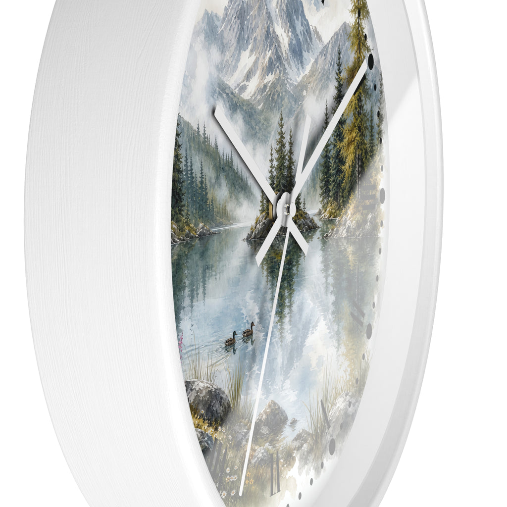 A round wall clock with a white textured frame and a scenic print of a mountain lake landscape featuring pine trees, ducks, and snowy peaks. The clock has white hands and is shown against a plain white background.