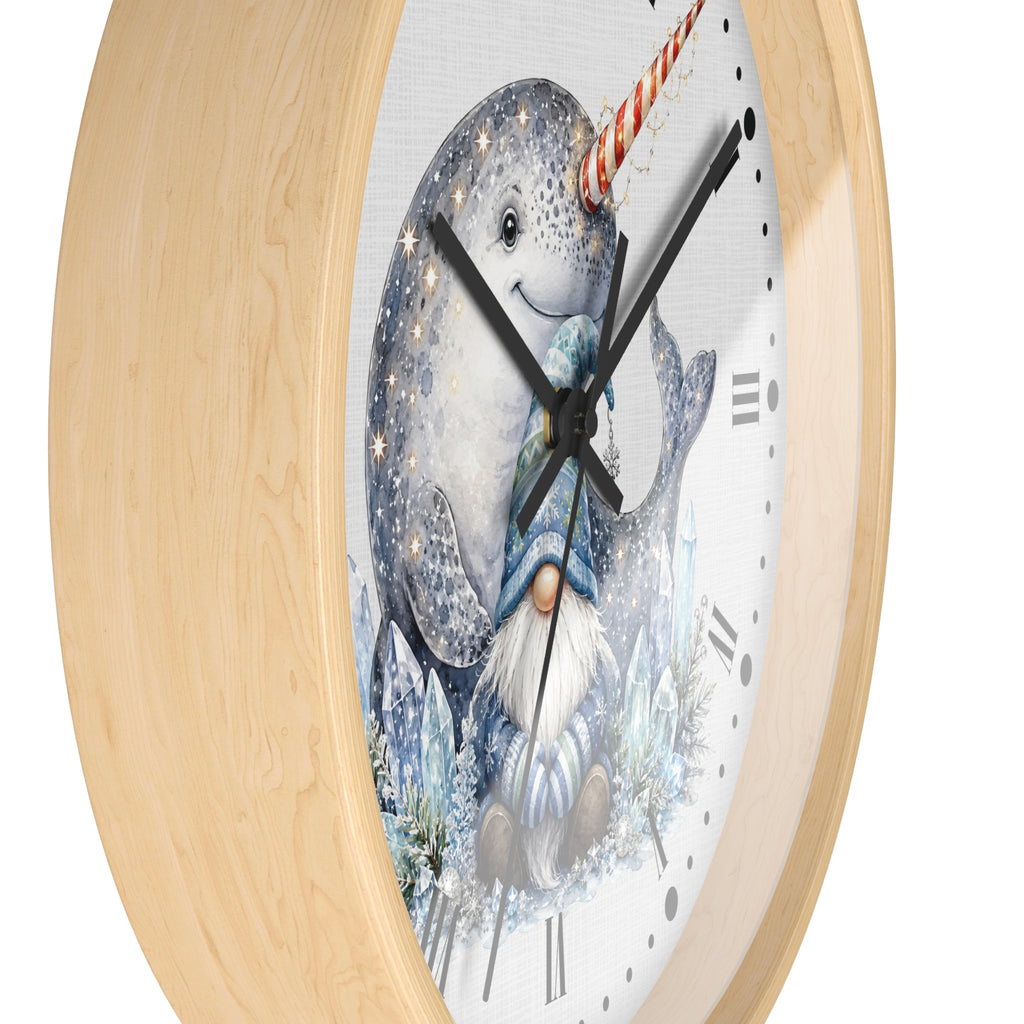 A round wall clock with a light natural wood frame and a white face featuring an illustration of a narwhal and a gnome in winter clothing, shown against a plain white background.