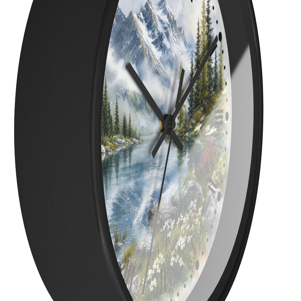 A round wall clock with a black frame and a scenic landscape print featuring a mountain lake, pine trees, and wildflowers. The clock is shown at an angle against a plain white background.