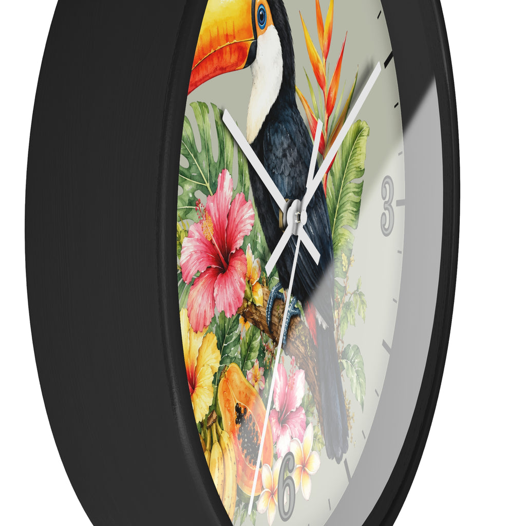 A close-up of a round wall clock with a black frame and a tropical design on the face, featuring a toucan, hibiscus flowers, and green leaves on a white background.