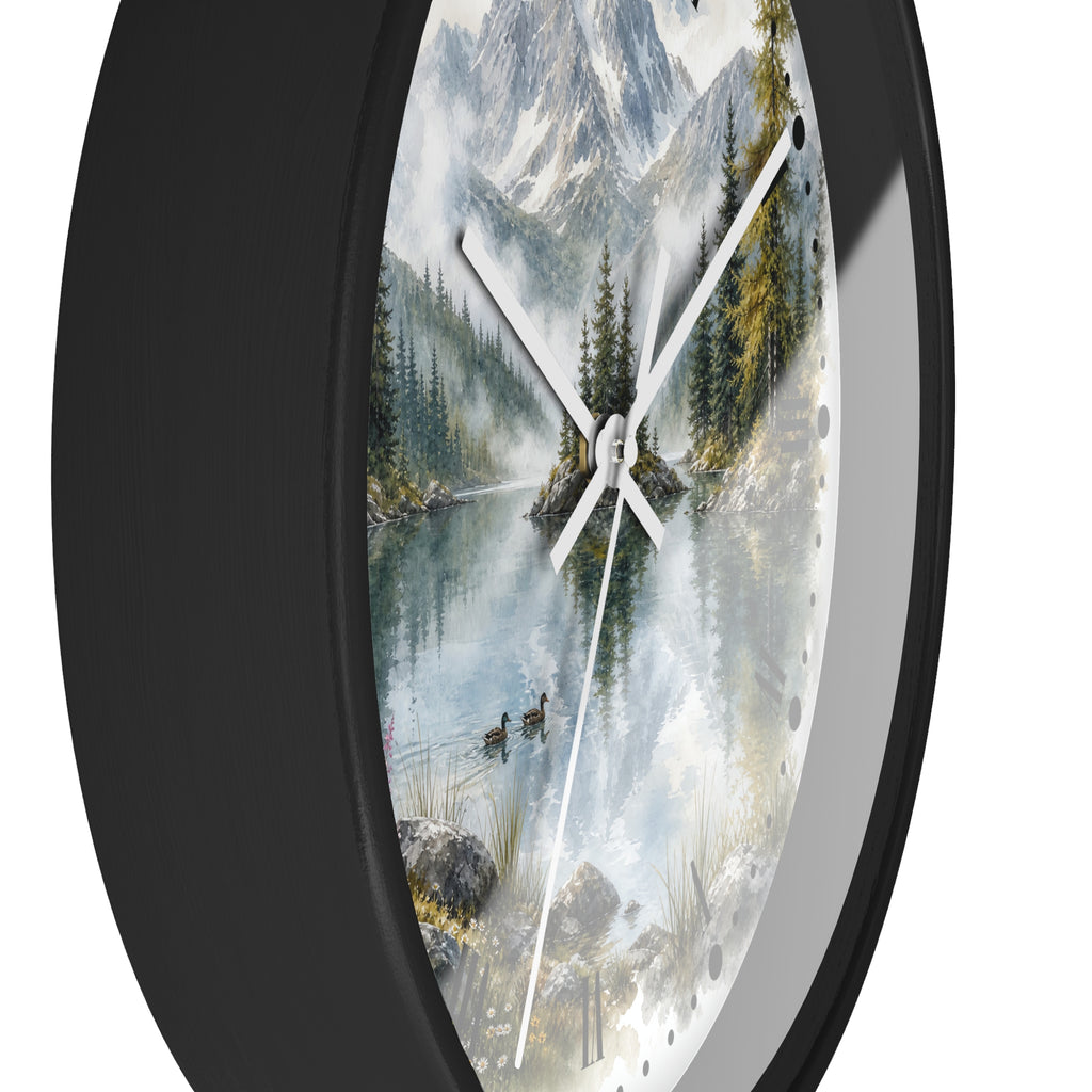 A round wall clock with a black frame and a scenic print of a mountain lake surrounded by pine trees, shown against a plain white background.