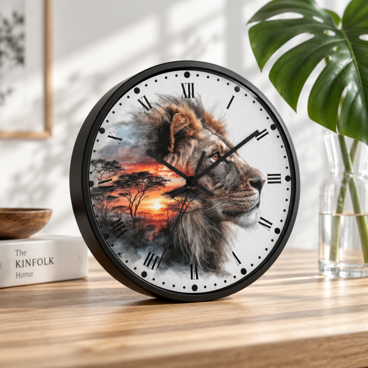 A round wall clock with a black frame sits on a wooden table. The clock face features a detailed lion portrait in profile with an African savanna sunset scene behind it.