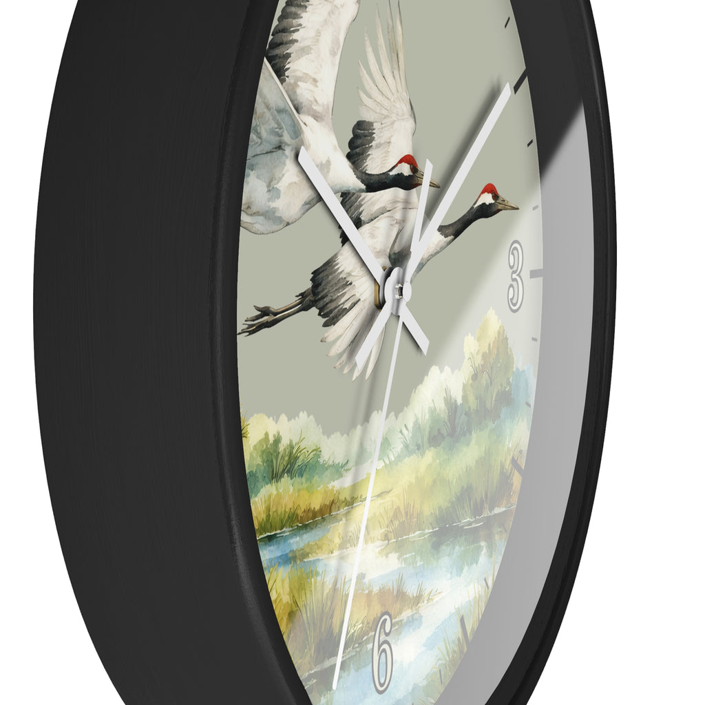 A close-up of a round wall clock with a black frame and a printed dial showing two flying cranes over a painted landscape. The clock has white hands and silver-tone numerals.