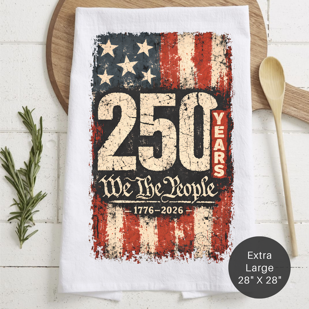 Tea towel with American flag design and '250 Years We The People' text on a wooden surface.