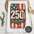 Tea towel with American flag design and '250 Years We The People' text on a wooden surface.