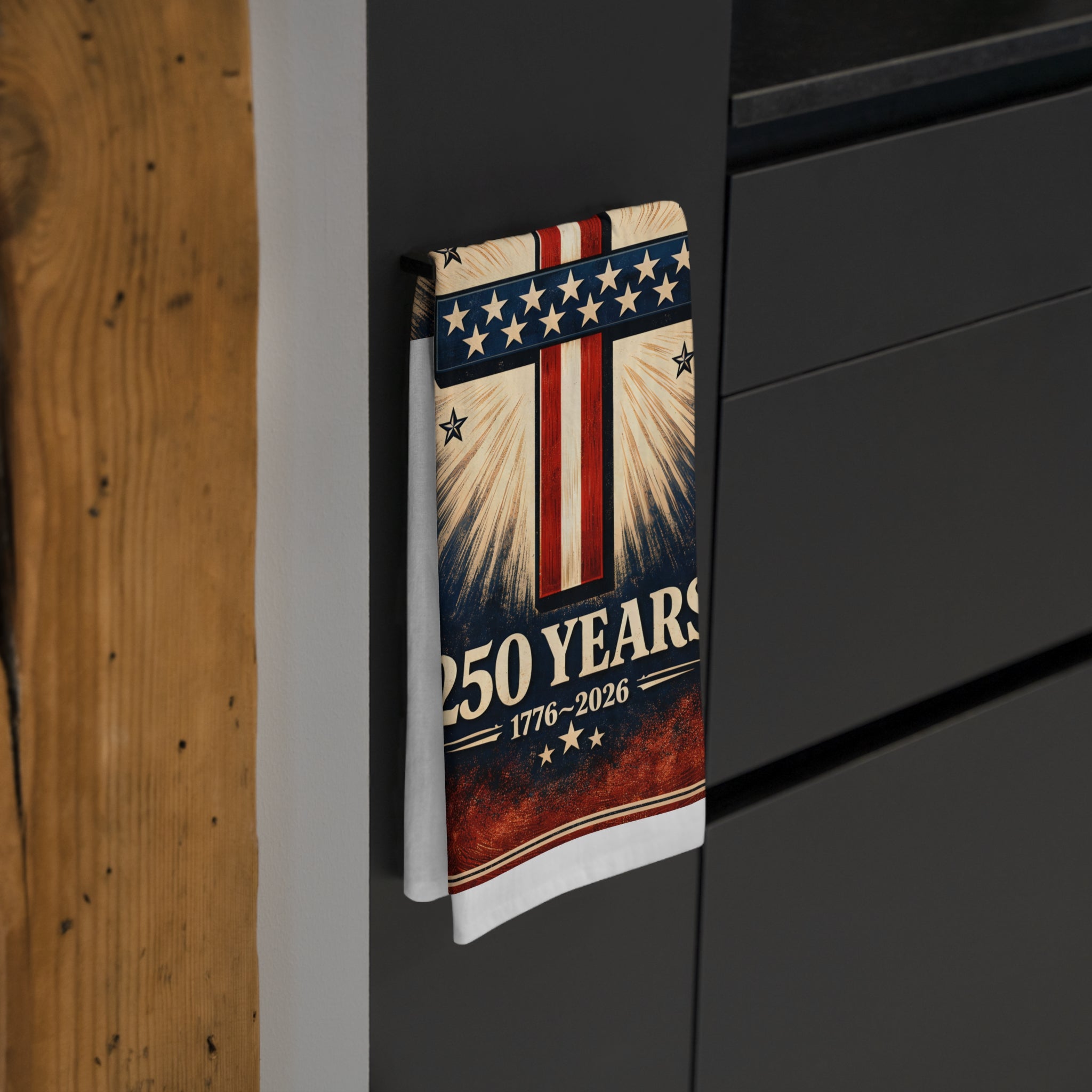 Tea towel with American flag design and '250 Years 1776-2026' text hanging on a dark cabinet.