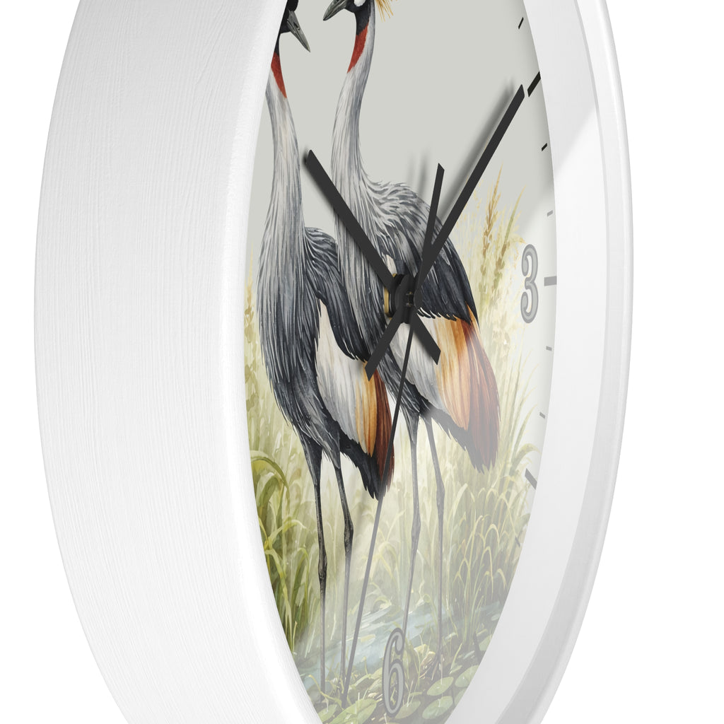 White round wall clock featuring a vintage-style illustration of two gray cranes standing in tall grass, with black hands and partial black numerals on a white face.