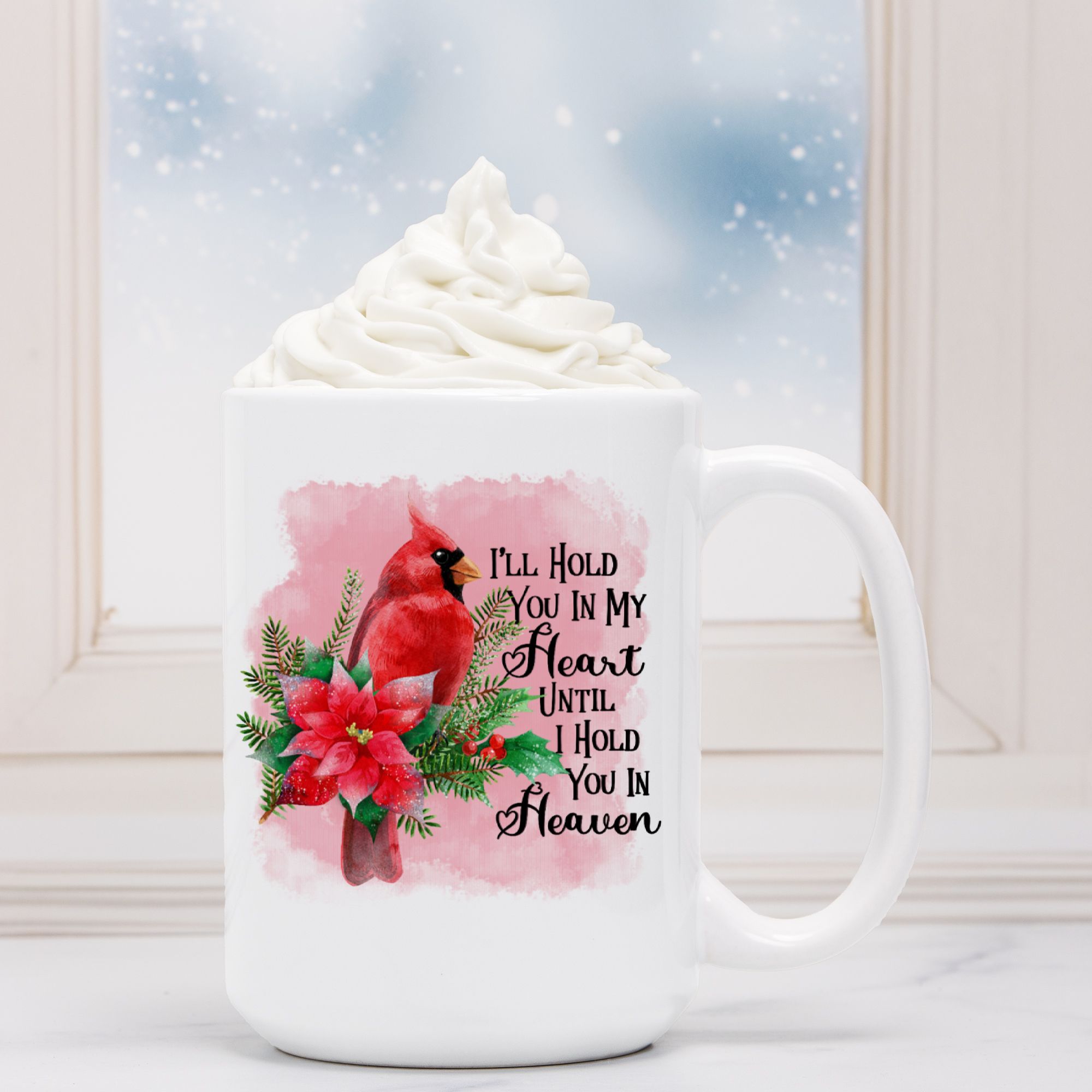 White mug with a red cardinal and floral design, text 'I'll Hold You in My Heart Until I Hold You in Heaven', against a snowy window background.