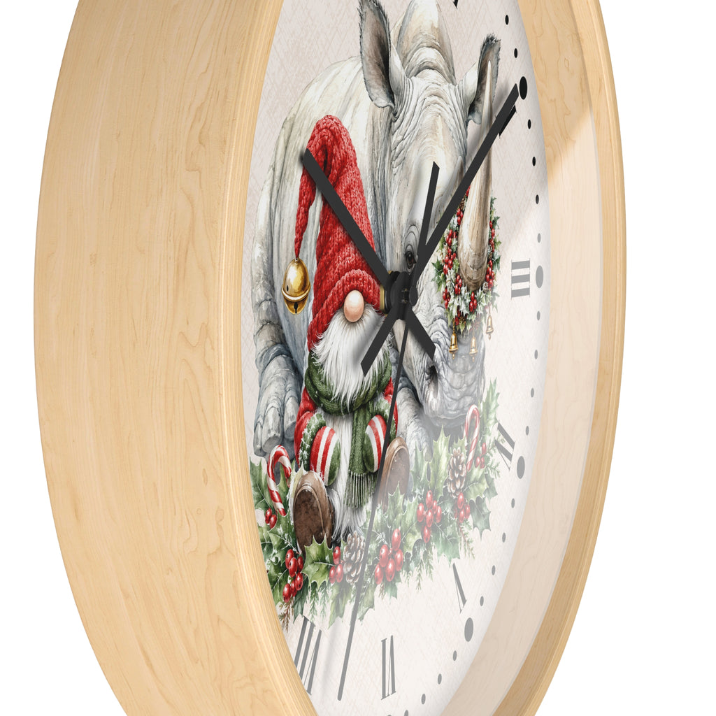 Round wall clock with a light natural wood frame and a white clock face featuring a festive illustration of a white rhinoceros wearing a red Santa hat and green wreath, with black hands and Roman numerals.