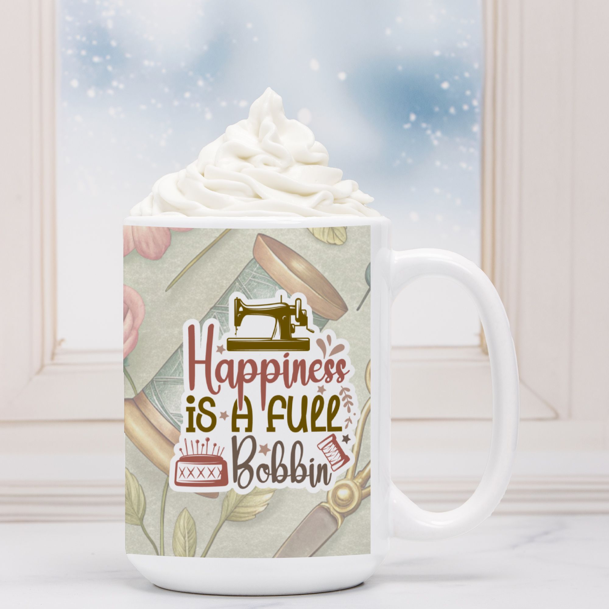White mug with sewing-themed design and 'Happiness is a Full Bobbin' text, filled with hot chocolate.