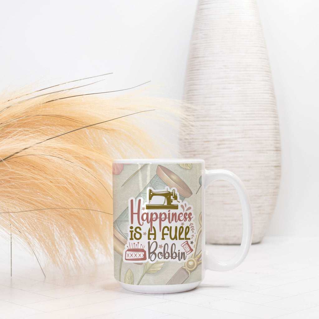 Mug with sewing-themed design and text 'Happiness is a full bobbin' on a white surface.