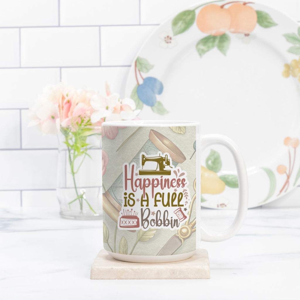 Mug with 'Happiness is a full bobbin' text and sewing-themed design, placed on a marble coaster with a plate and flowers in the background.