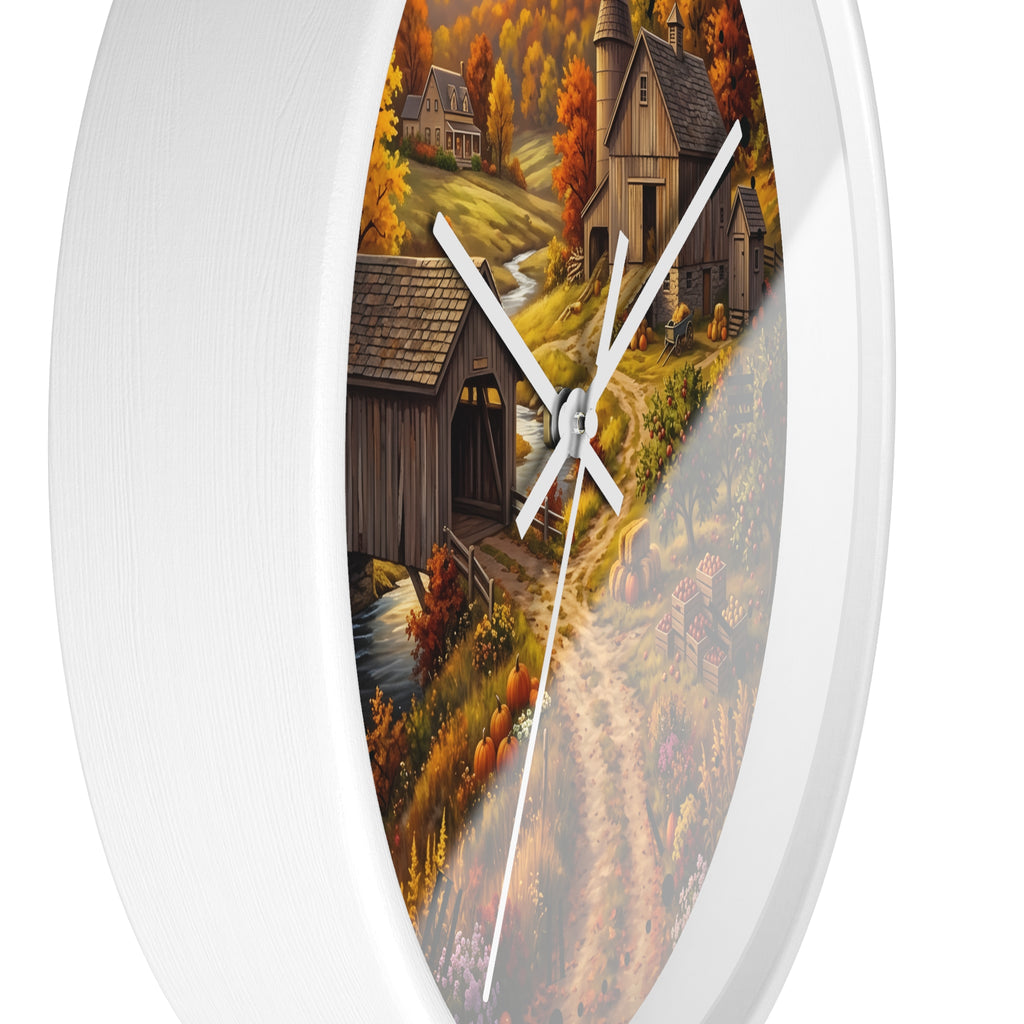 Round wall clock with a white frame and a printed autumn countryside scene featuring rustic cabins, a covered bridge, a stream, and colorful fall foliage. The clock face is partially obscured by a diagonal gray overlay.
