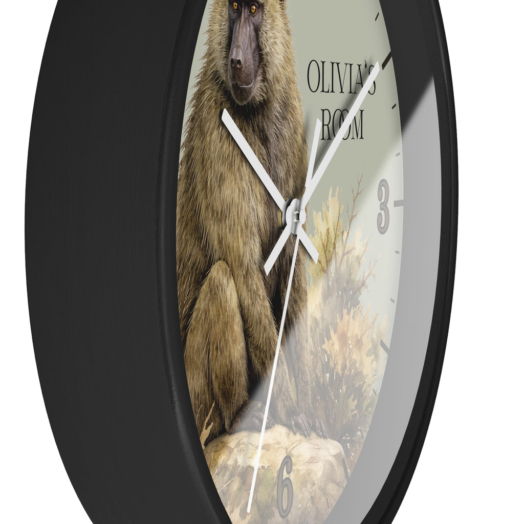 A round wall clock with a black frame and a printed dial featuring a brown baboon illustration, white clock hands, partial black numerals, and the text 'OLIVIA'S ROOM'.
