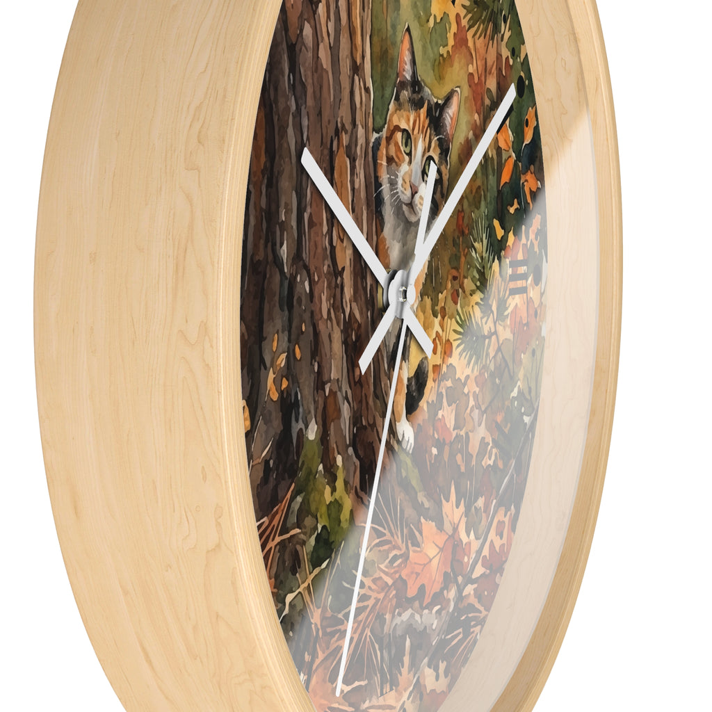 Round wall clock with a light natural wood frame and a printed artwork of a calico cat peeking from behind a tree in an autumn forest.