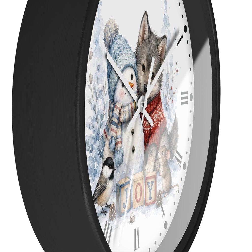A round wall clock with a black frame and a white face featuring a winter illustration of a snowman, a wolf, a bird, and the word "JOY" in colorful blocks.