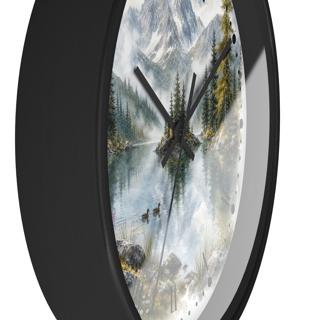 A round wall clock with a black frame and a scenic landscape print on the face, showing a misty mountain lake with pine trees, ducks, and snow-capped peaks. The clock is photographed against a plain white background.