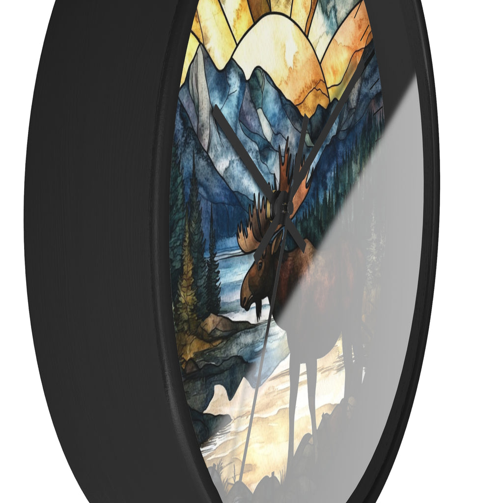 Round wall clock with a black frame and a stained-glass-style nature print featuring a moose, mountains, trees, and a yellow sun, shown against a white background.