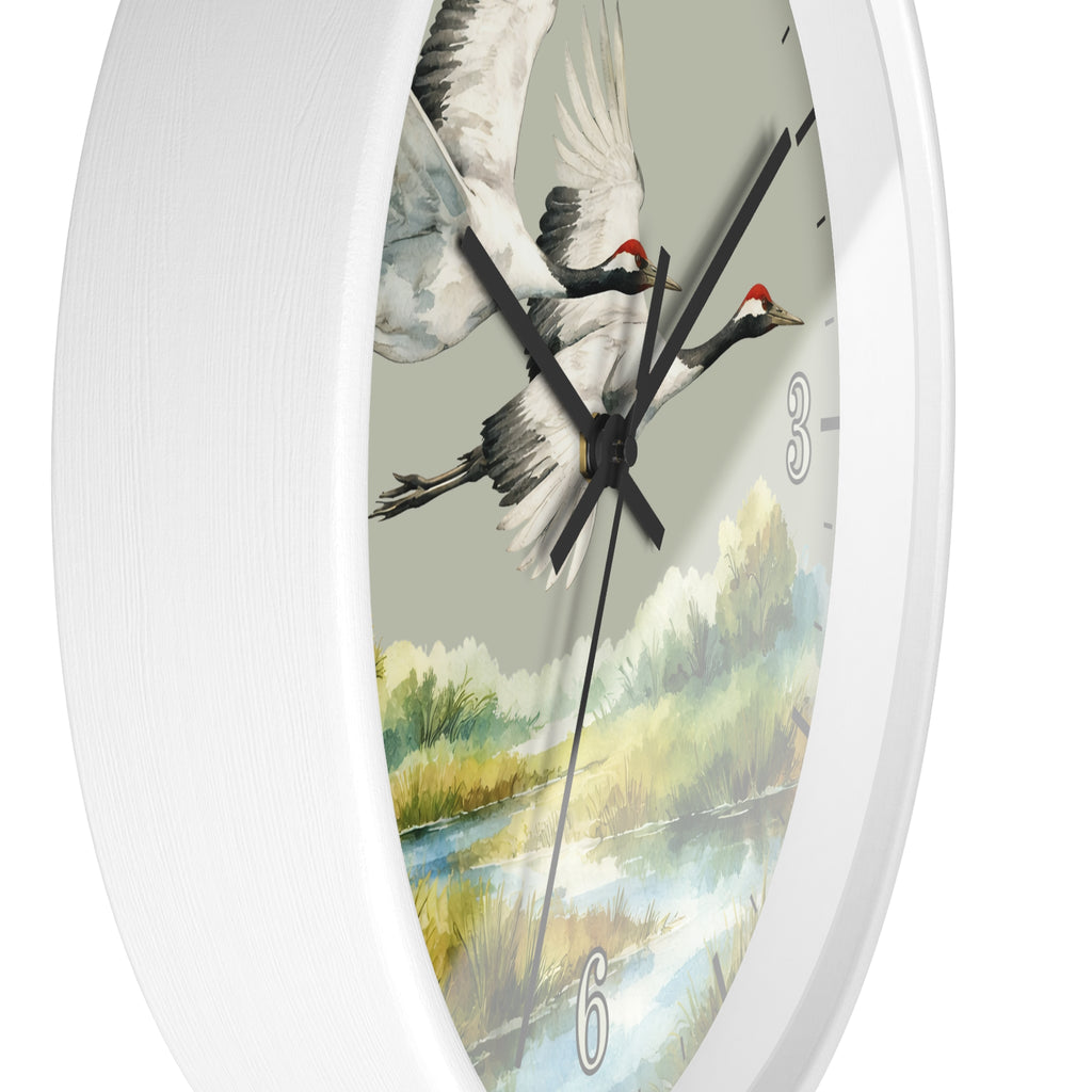 A white oval wall clock featuring a painted scene of two flying cranes over a river landscape, with black hands and silver numerals.