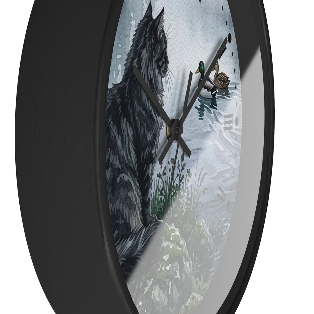 A round wall clock with a black frame and black hands, featuring a printed illustration of a black cat on a snowy outdoor scene. The clock is shown cropped at an angle against a plain white background.