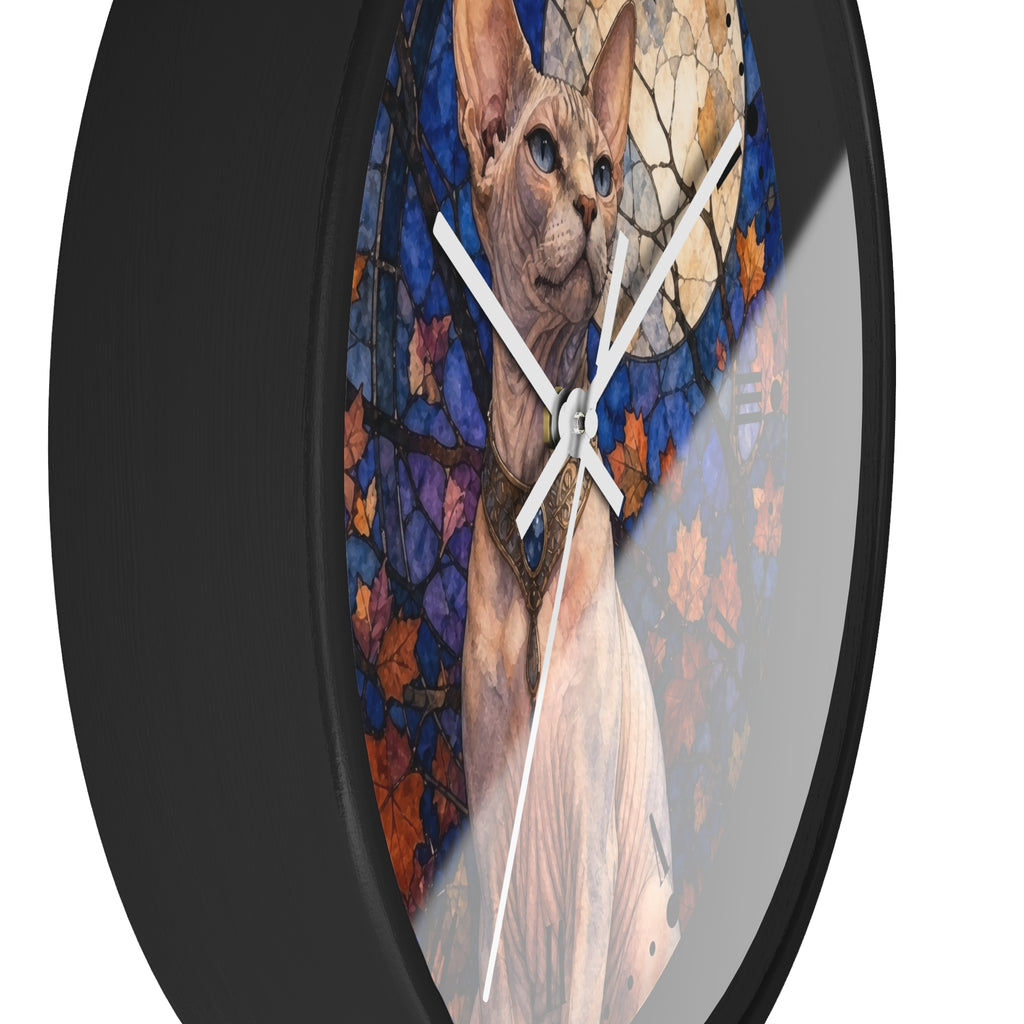 Round wall clock with a black frame and a printed design of a Sphynx cat in front of a stained-glass-style autumn scene with blue, purple, orange, and beige tones.