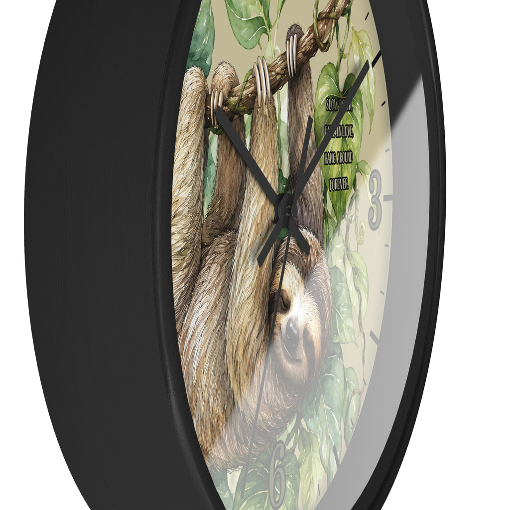 A round wall clock with a black frame and a printed face showing two sloths hanging from a tree branch among green leaves. The clock has black hands and black numerals, photographed against a plain white background.