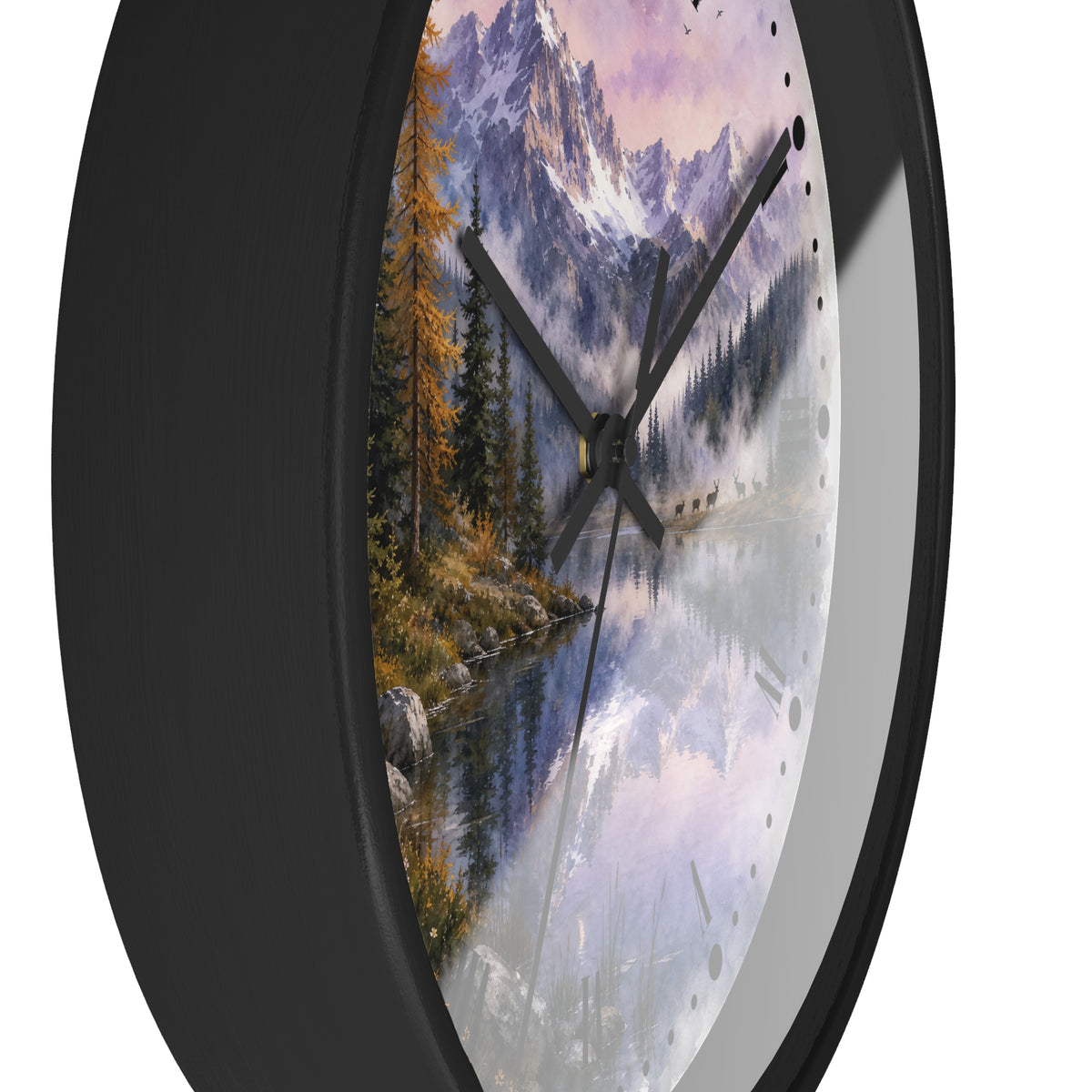 A round wall clock with a black frame and a scenic landscape print on the face showing mountains, pine trees, a herd of deer, and a reflective lake, photographed against a plain white background.
