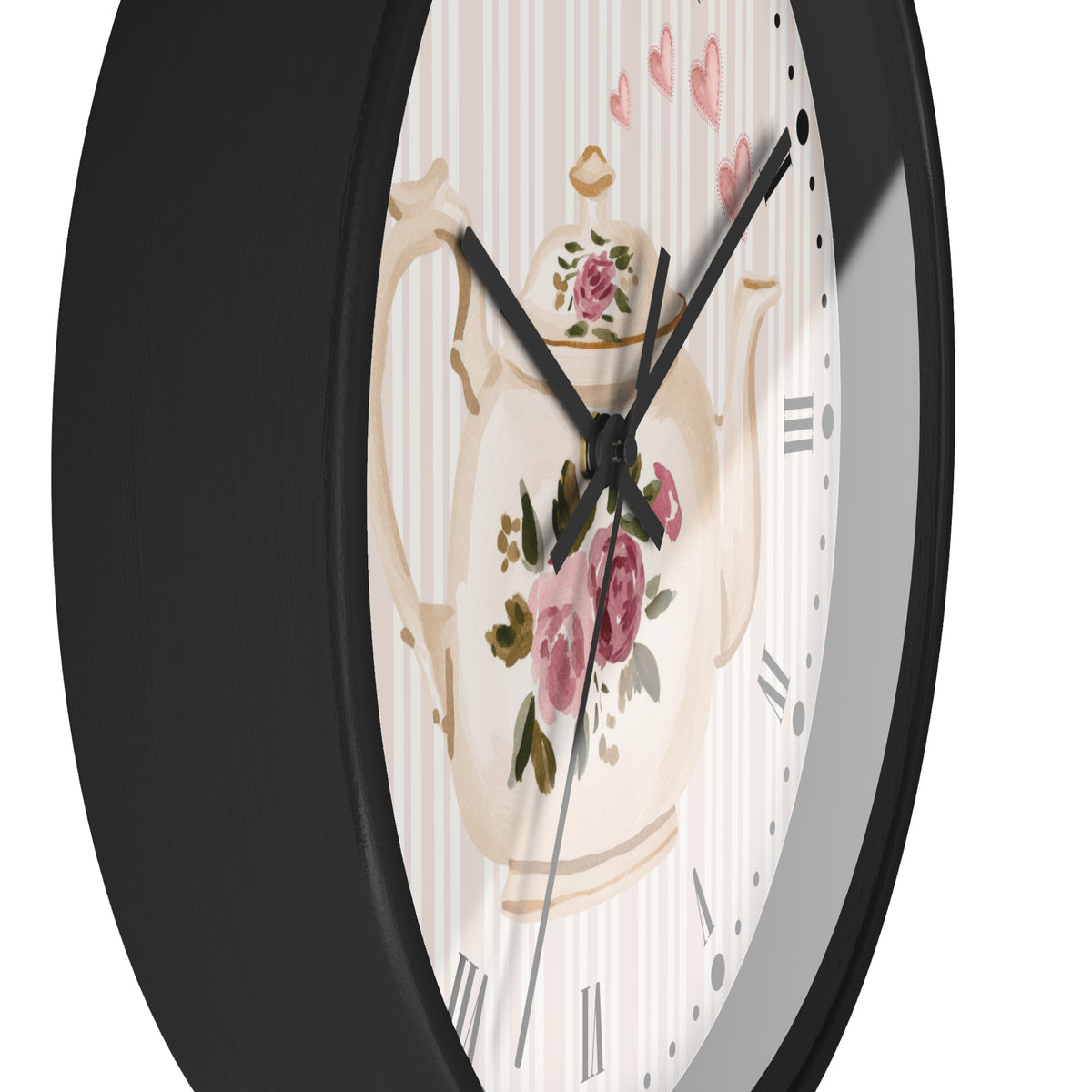 A close-up of a round wall clock with a black frame and a decorative dial featuring a cream teapot illustration with pink flowers and striped background.
